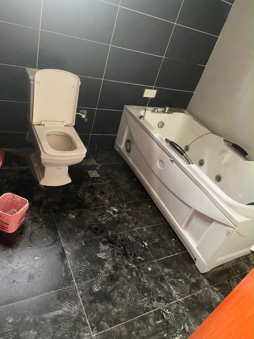 Bathroom with heavily soiled dark tiles, stained toilet and bathtub before deep cleaning